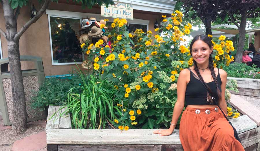 The author smiling for a photo in Taos Plaza with colorful flowers on her background