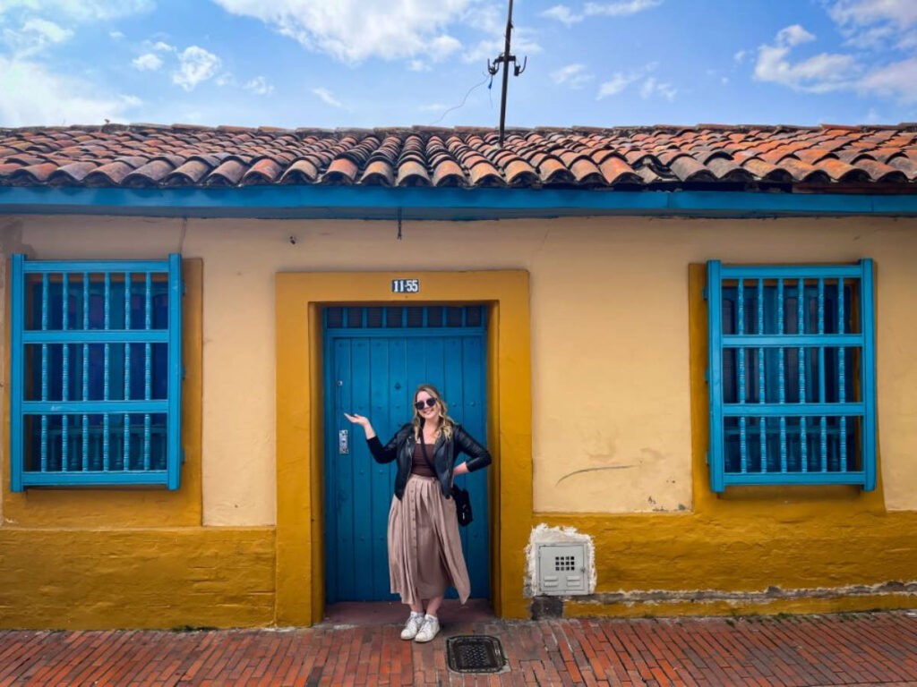 The author Taylor Herperger posing for a photo with a colorful house