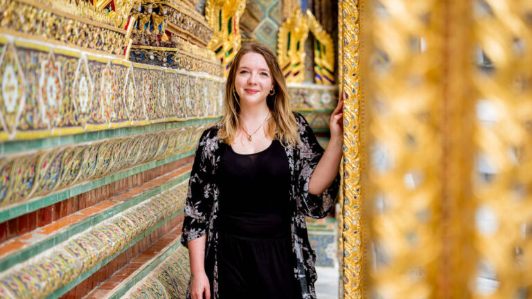 The author Taylor Herperger, posing for a photo at the intricate and golden interior of Grand Palace in Bangkok