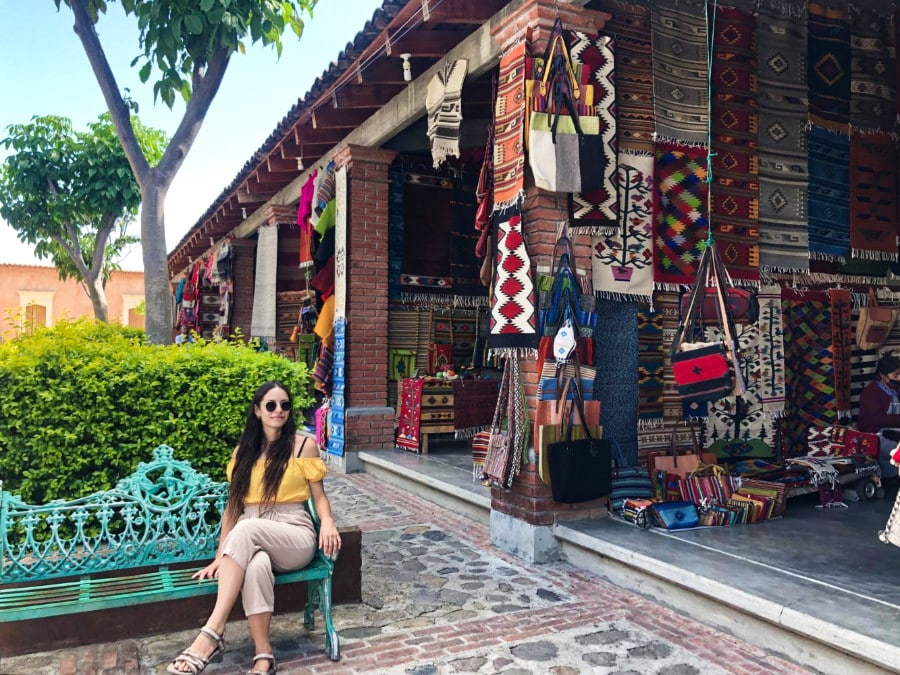 The author McKenna Mobley posing on a bright light blue iron chair near the handcrafted Oaxacan textiles shop