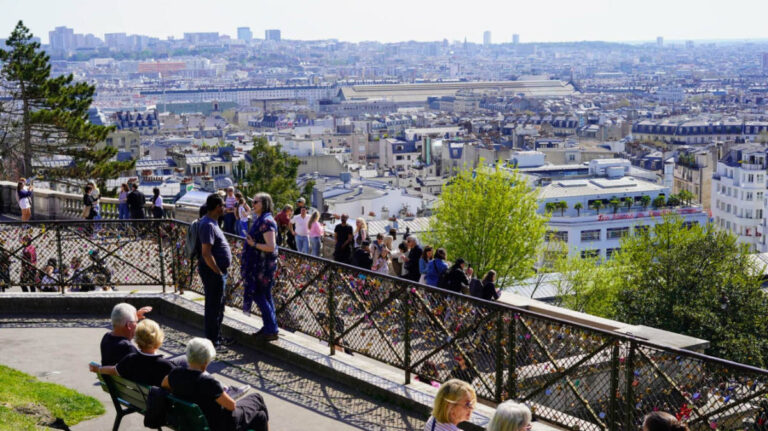 Visitors gather along a love lock-covered railing at the Montmartre overlook near Sacré-Cœur Basilica
