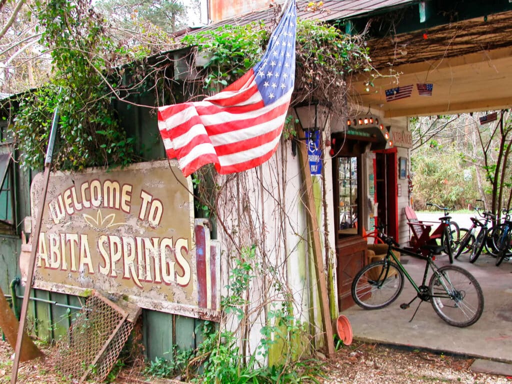 View of the welcome signage of Abita Springs with the US flag near the entrance of Abita Mystery House