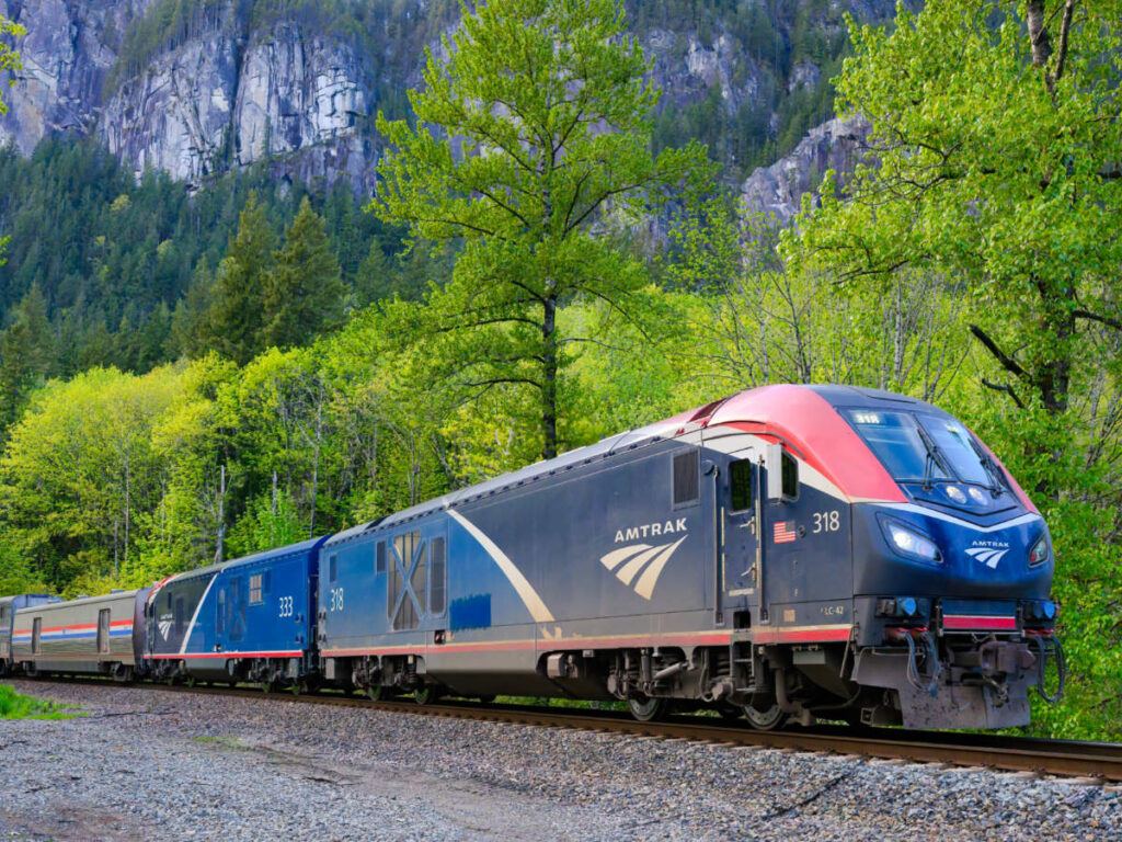 View of the Amtrak Empire Builder passenger train in Cascade Mountain Range surrounded by green trees