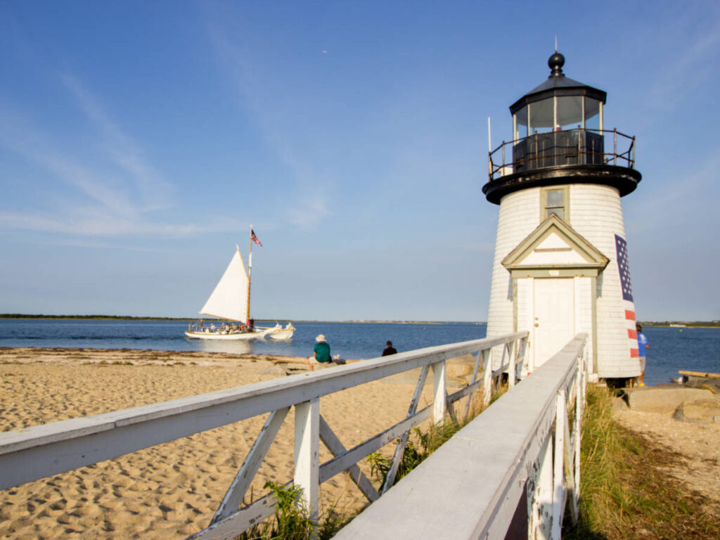 View of the boardwalk leading to Brant Point Lighthouse with a sailing catamaran in the background