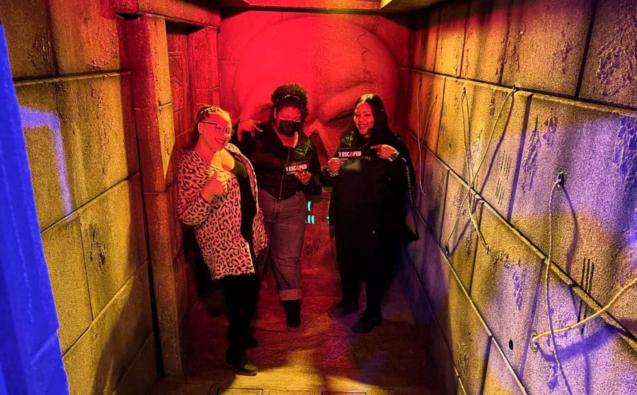 The author Seychelle Thomas and her sisters posing inside The Escape Room with stone walls around