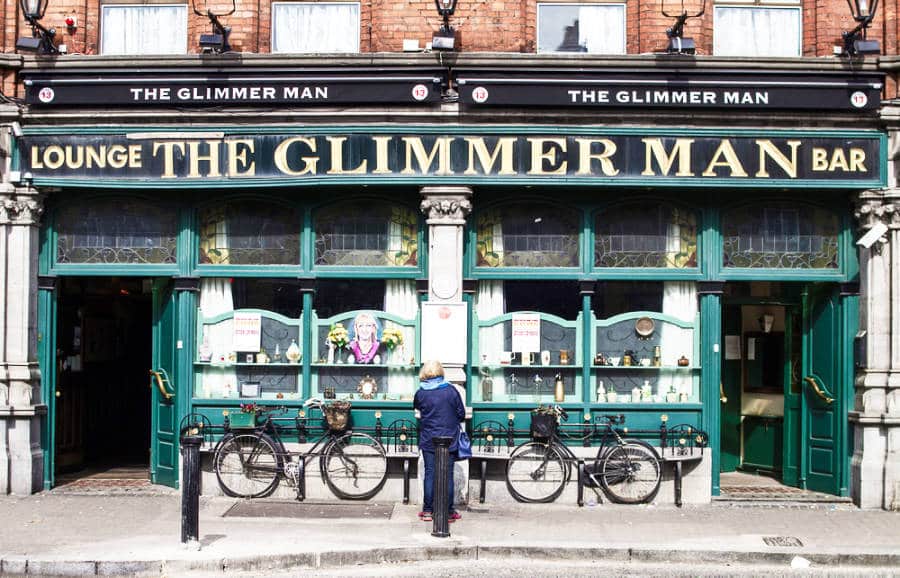 An old woman standing outside The Glimmer Man Pub on a sunny day