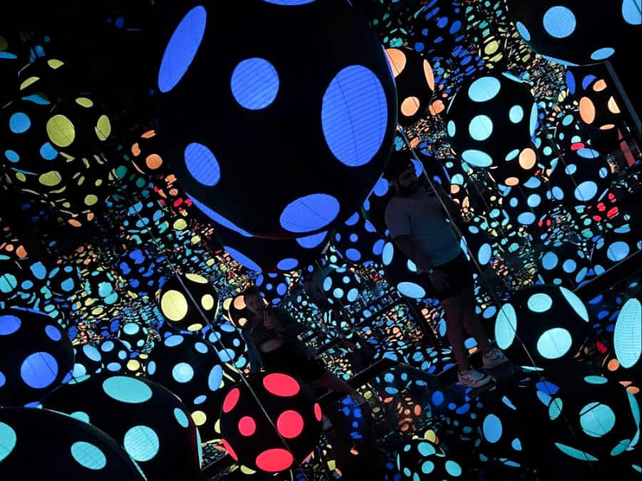 The author Seychelle Thomas and her partner inside the dark room of infinity mirrors with illuminated colorful balls with polka dots