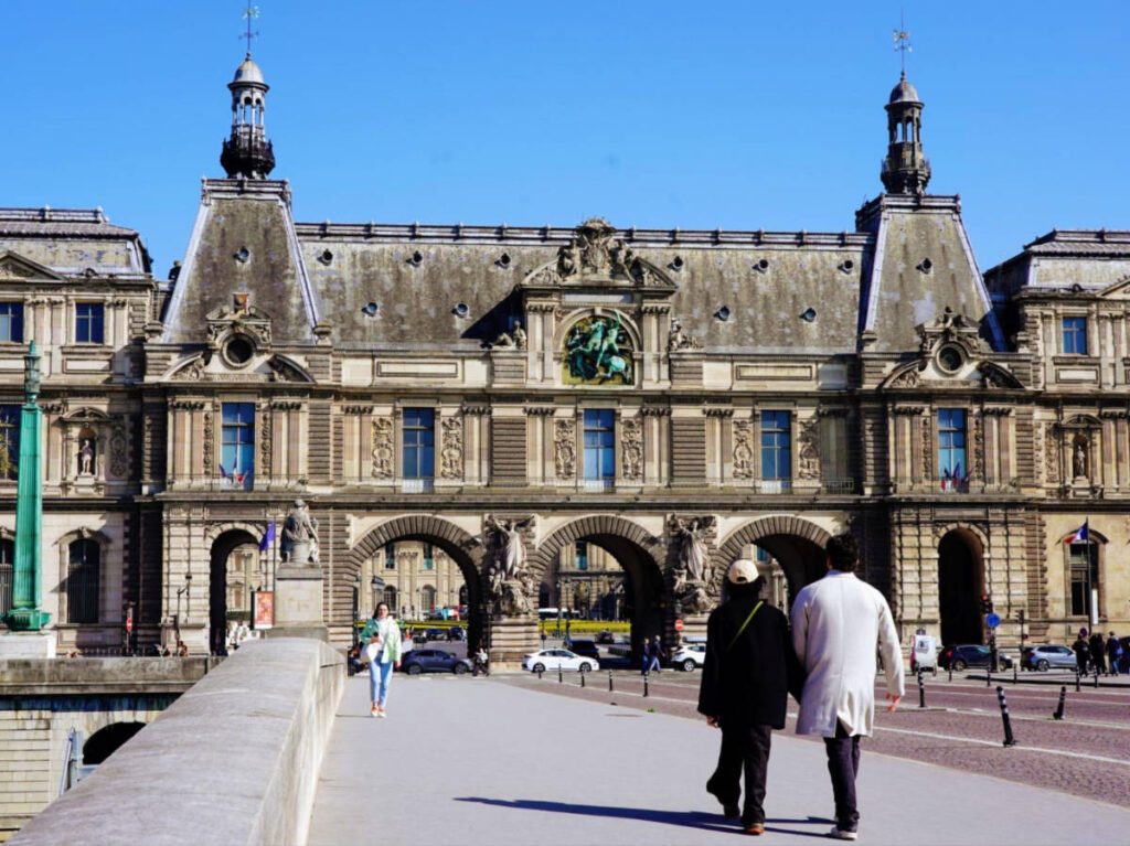 People walk along Pont du Carrousel towards Louvre Palace in Paris