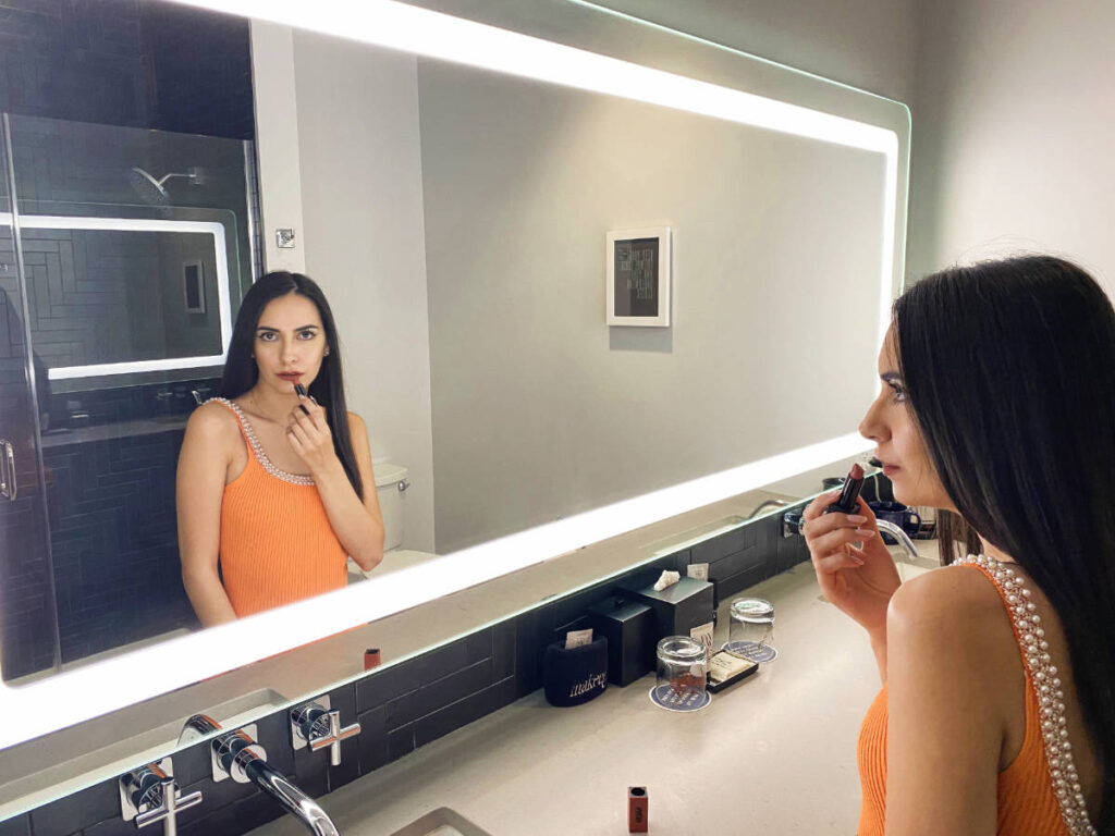 Clara Kesseler putting a lipstick in front of a big mirror on their bathroom in The Maven Hotel Denver