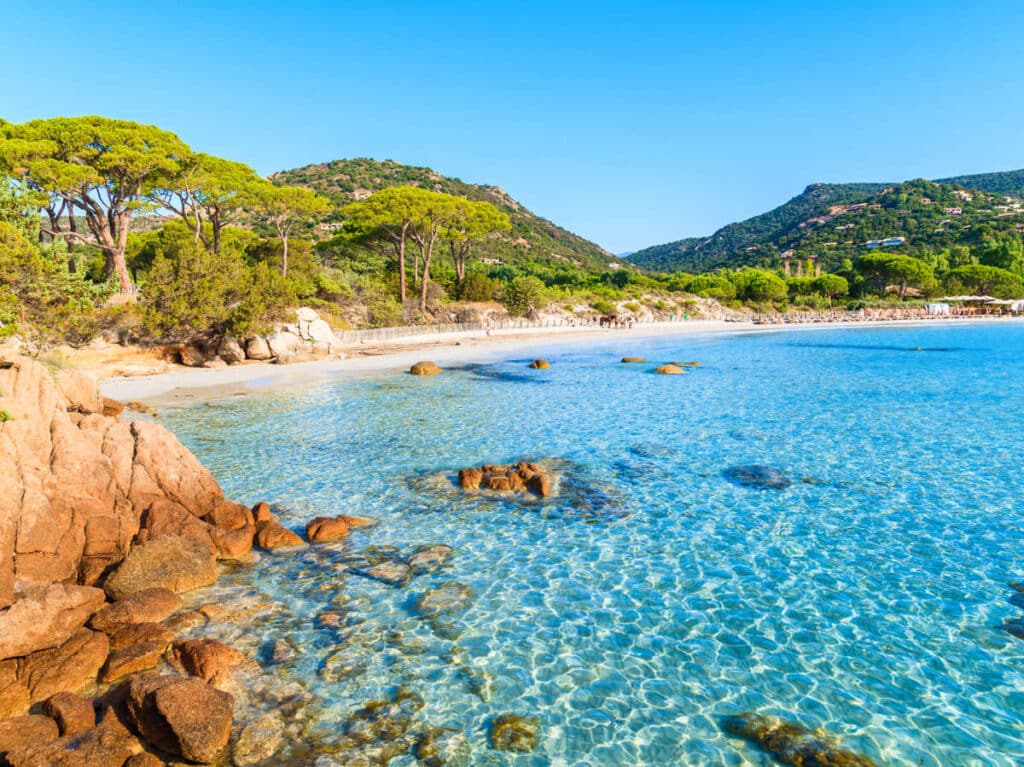 View of the clear blue water surrounded by rocky shoreline with greenery in Palombaggia Beach