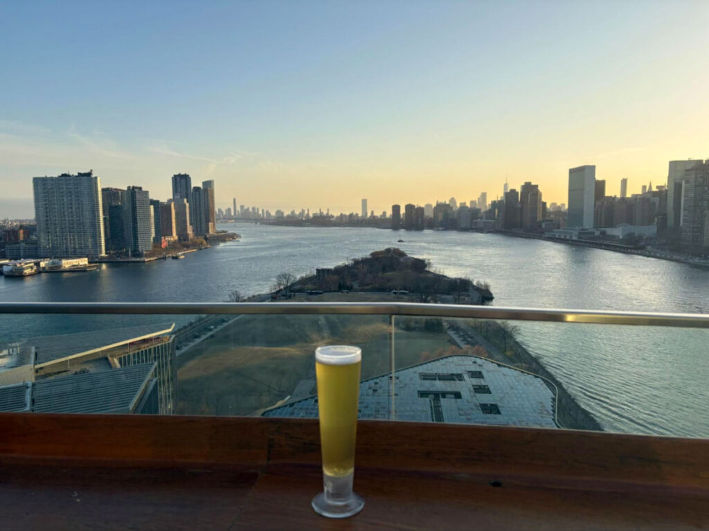 A tall glass of beer at the Panorama Room, overlooking the East River with sunset views of Manhattan’s skyline