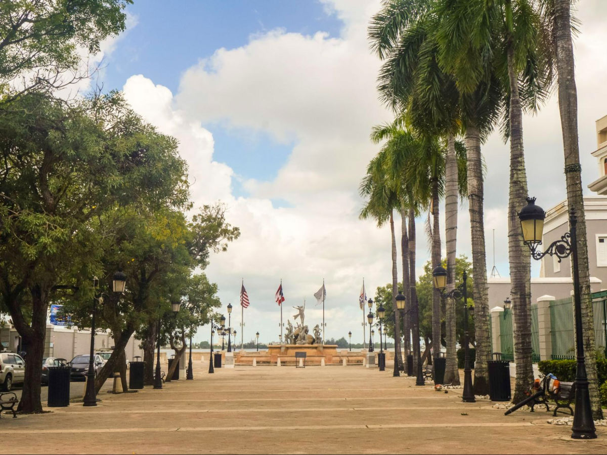 Trees and benches at The Paseo de la Princesa with flags and statue in the background