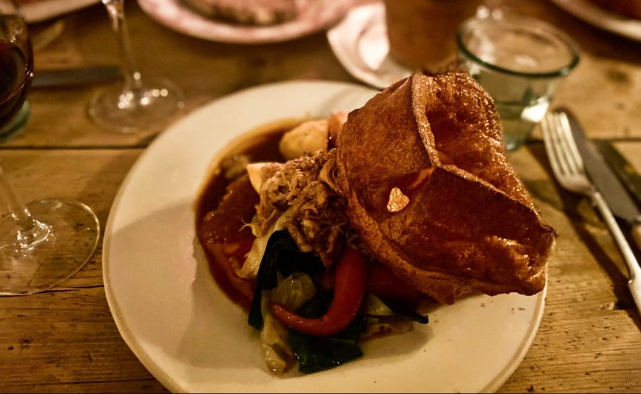 A plate of pulled pork and vegetables on the side with glasses of wine on the table at The Pig’s Head