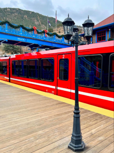 Red train of the Pikes Peak Cog Railway awaits passengers on a platform