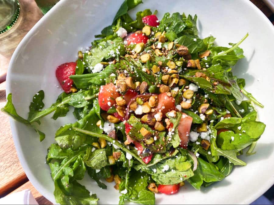 A bowl of strawberry arugula salad with rosted pistachios and feta cheese