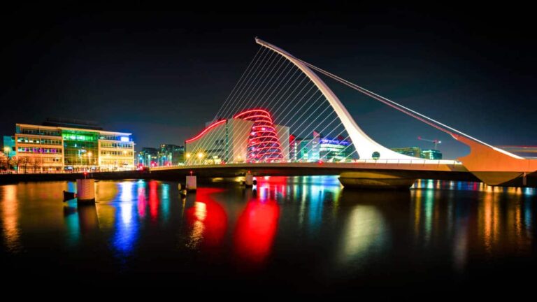 View of the Samuel Beckett Bridge and the illuminated city skyline reflected on the water at night