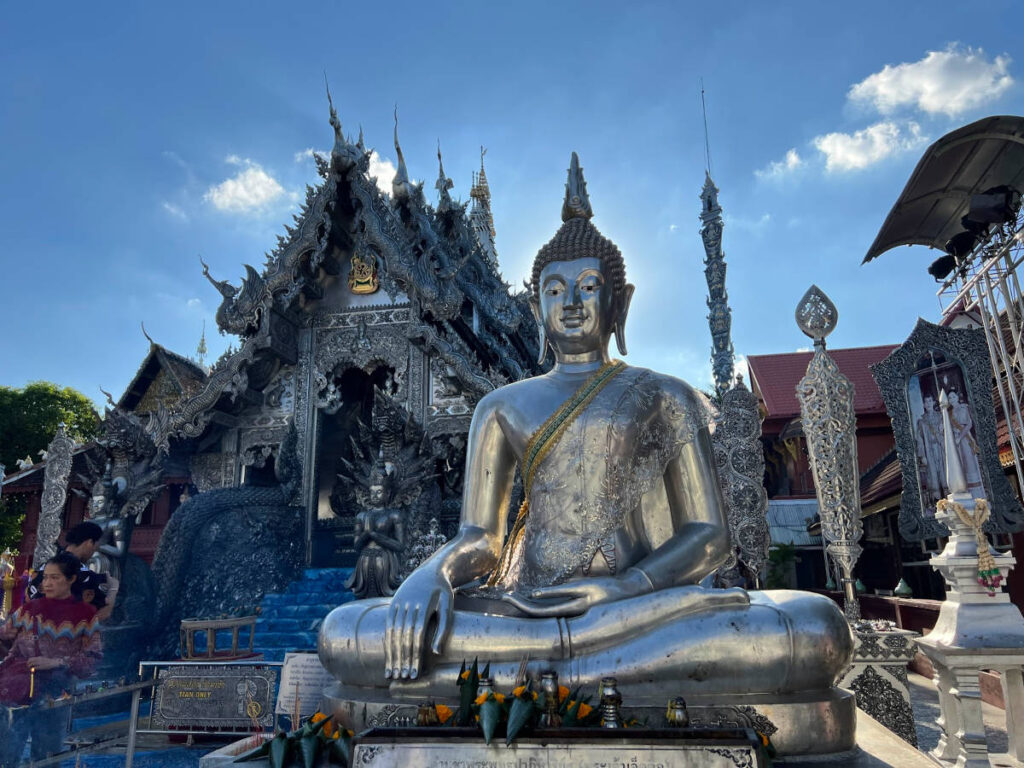 A large silver Buddha statue stands in front of Wat Sri Suphan temple