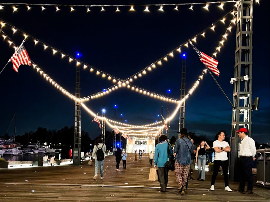People strolling at the boardwalk with illuminated stringed lights above at night