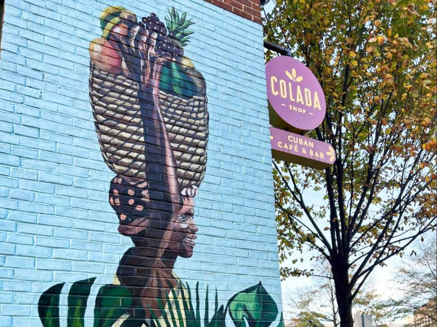 A mural of a woman holding a basket of fruits above her head at the Colada Shop