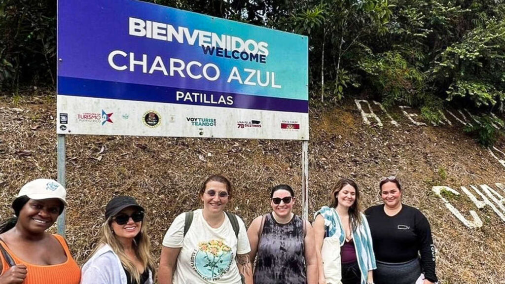 Group of tourists smiling for a photo in front of the signage of Charco Azul