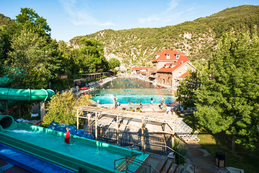 View of the people enjoying the pool and slide in Glenwood Hot Springs Resort with the beautiful mountain in the background on a sunny day