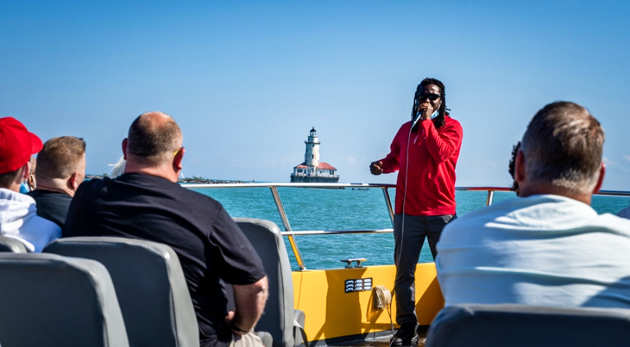 A tour guide speaking in front of the tourists o the SeaDog boat with the Chicago Harbor Lighthouse view