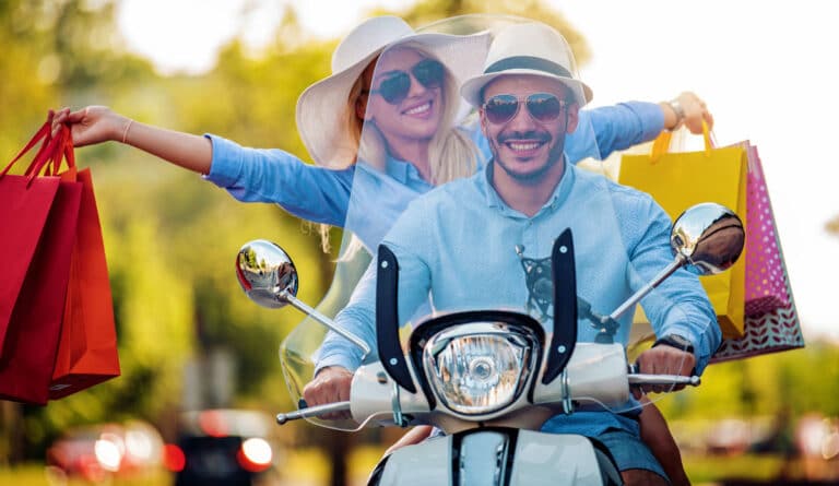 View of couple riding a motorcycle holding shopping bags showing some of the best travel gifts for couples