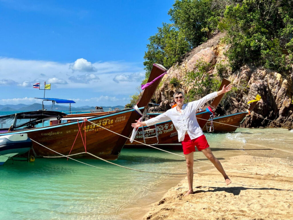 Travel Lemming Founder Nate on the beach near the long boats at Koh Phakbia
