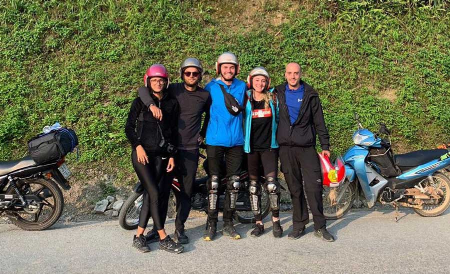 A group of people smiling for a photo with their motorbikes on their background
