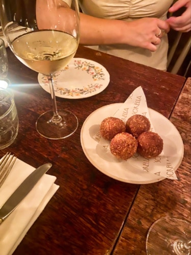 A plate of Truffle Arancini with a glass of white wine on the sine in Sorella