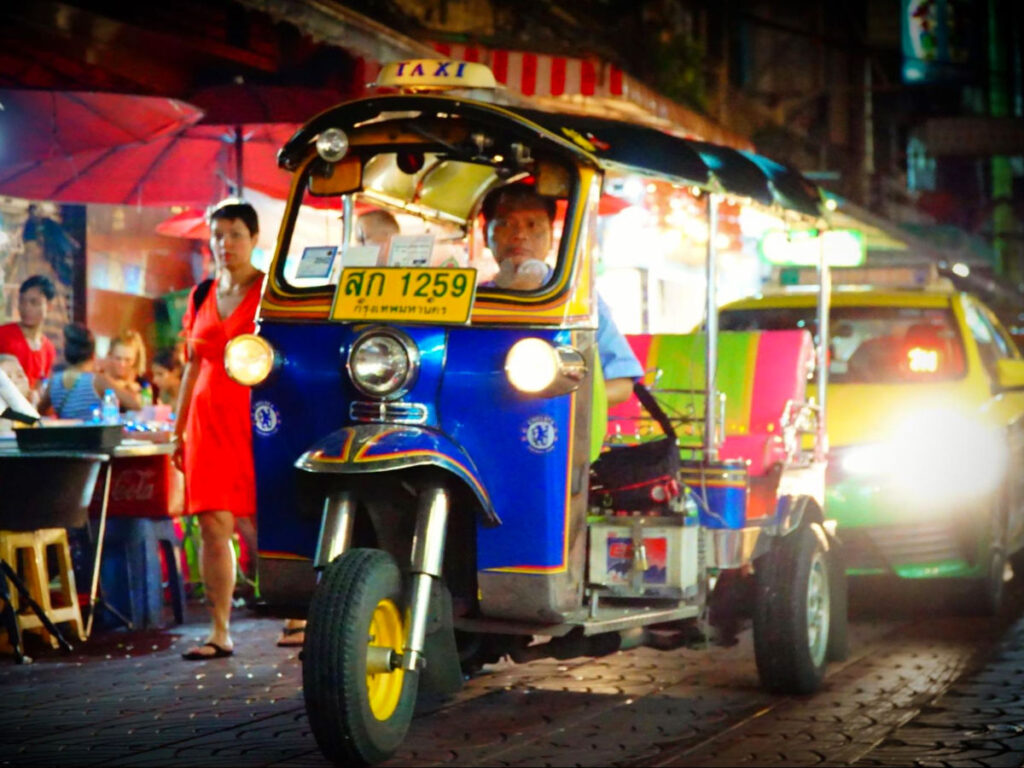A man drives a tuk tuk along a lively Chinatown street