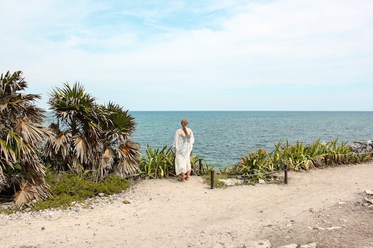 Taylor in front of the ocean with tropical plants near the Tulum Ruins in Mexico