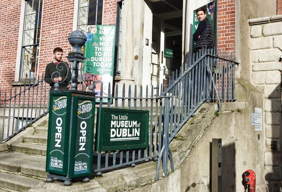 Two men standing at the entrance of the Little Museum of Dublin on a sunny day