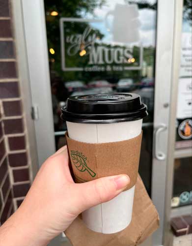 The author holding her cup of coffee and the Ugly Mugs Coffee & Tea entrance of the background
