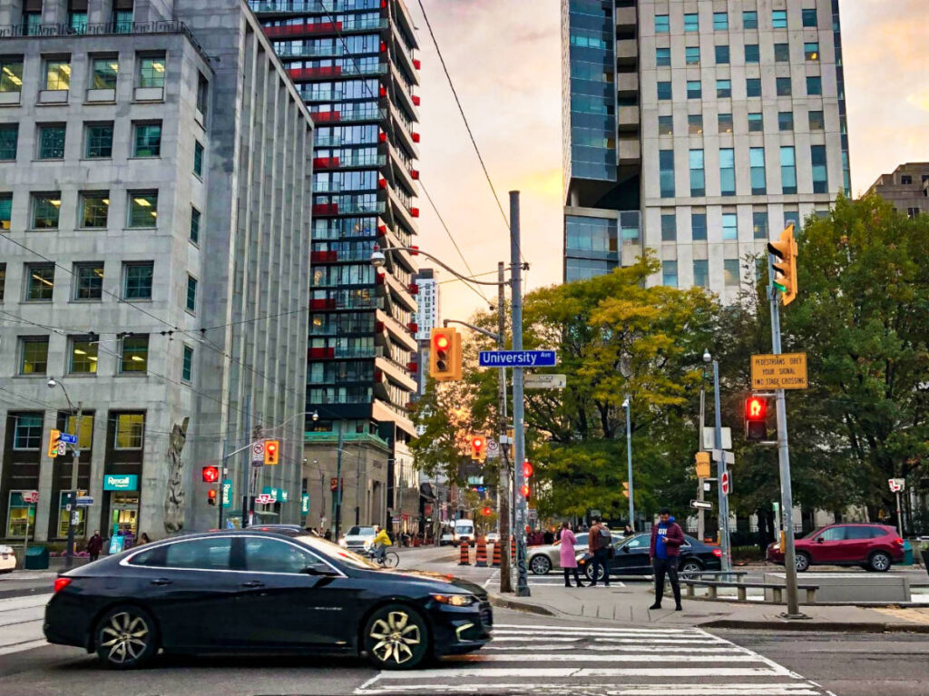 View of the people walking along the University Avenue with the buildings, cars and traffic lights around at sunset