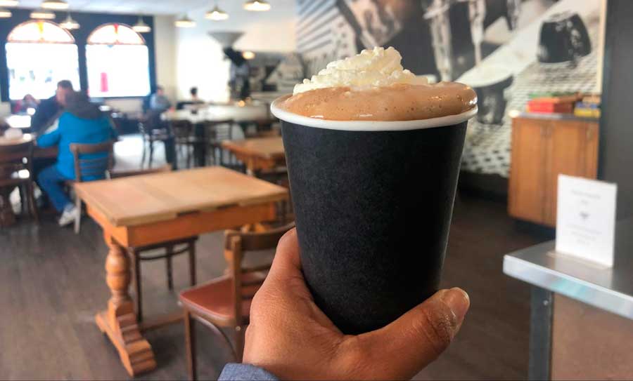 The author holding a cup of latte with velvet foam on top in Uptown Espresso
