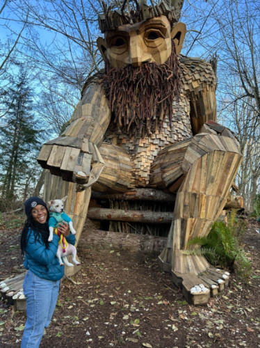Author Chelsea posing for a photo with Vahon’s resident troll sculpture while holding her dog