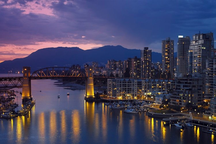 Vancouver, British Columbia at dusk with the sun setting in the background and city lights reflecting on the water