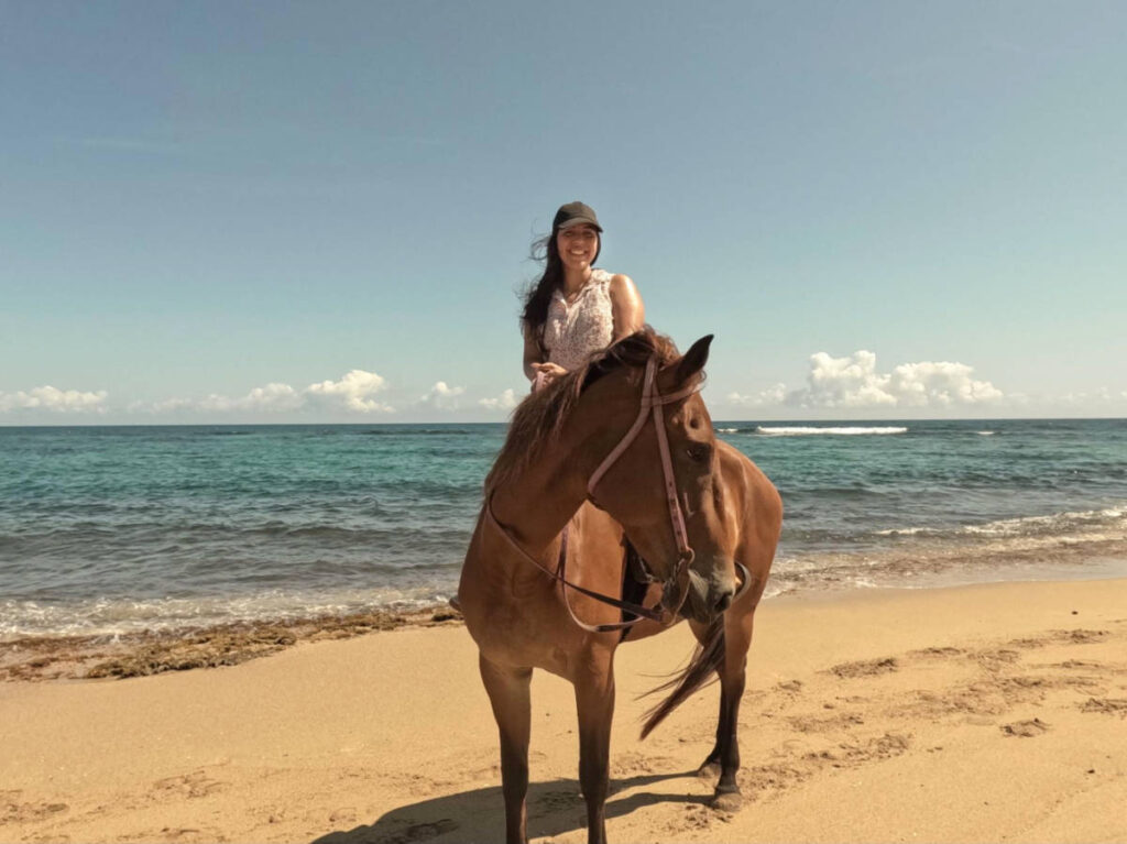 The author Vanessa Ramos posing for a photo while riding the horse along the shoreline