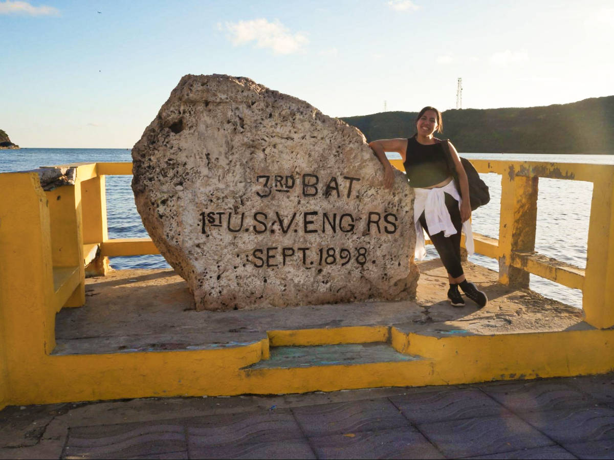 The author Vanessa Ramos, standing beside the big rock with inscription on it in El Malecón