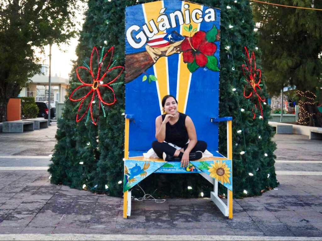 Thea author Vanessa Ramos, sitting on a huge chair in front of the Christmas Tree in Guánica