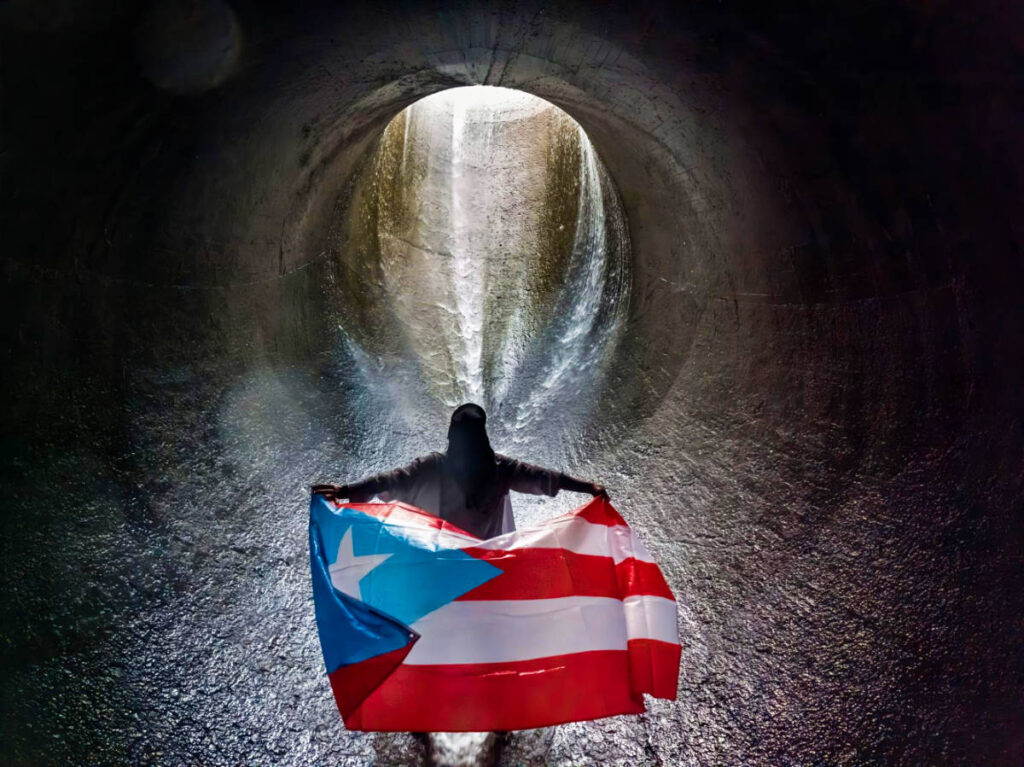 The author Vanessa Ramos, holding the flag of Puerto Rico under the overflow funnel in Lago Las Curias