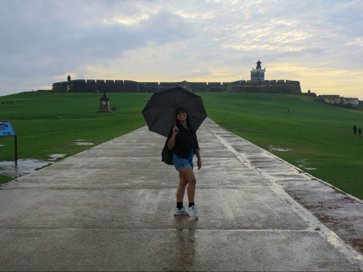 The author Vanessa Ramos holding an umbrella in front of Castillo San Felipe del Morro