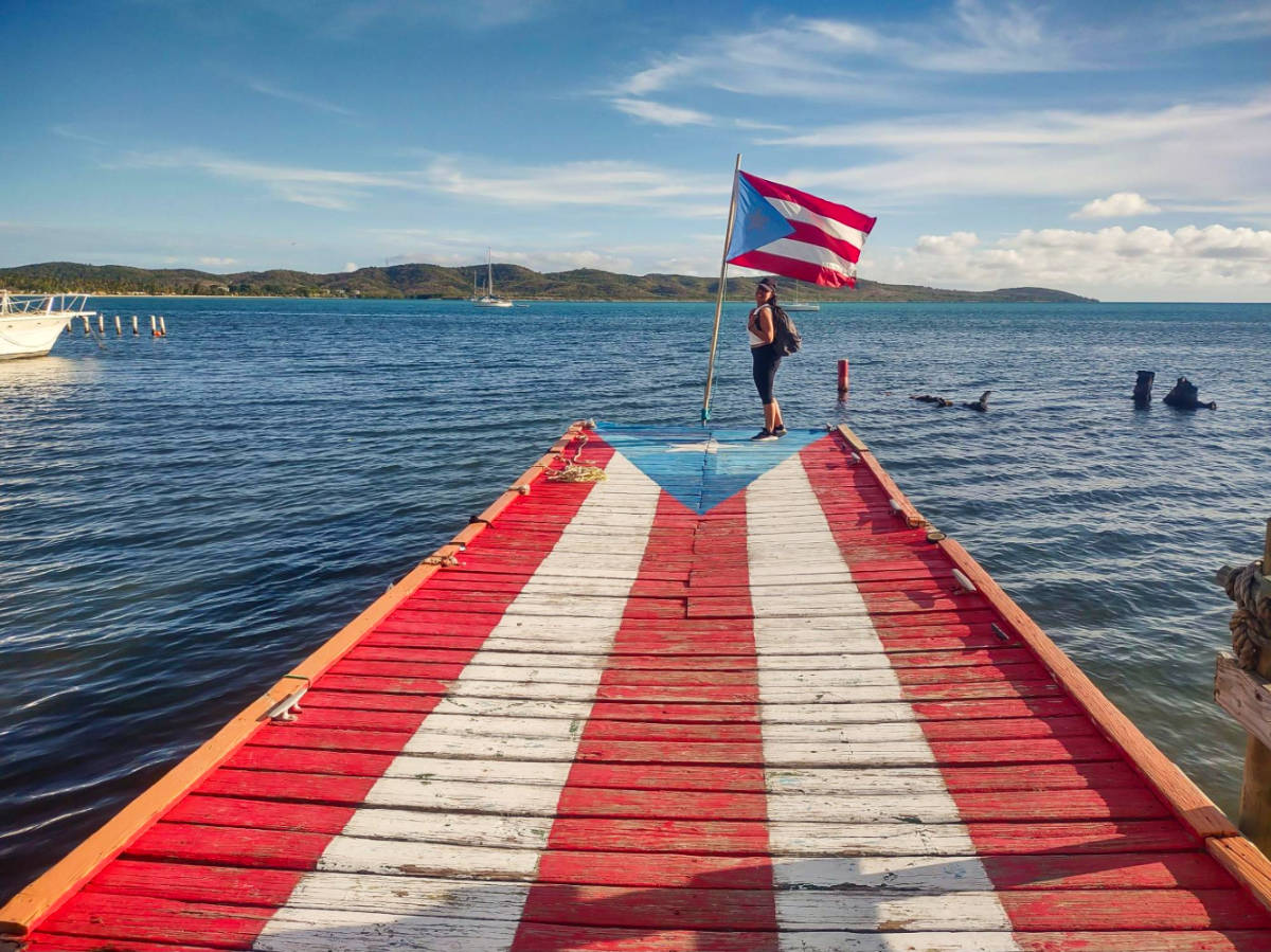 The author, Vanessa Ramos posing for a photo with the flag of Puerto Rico at the Muelle de la Libertad
