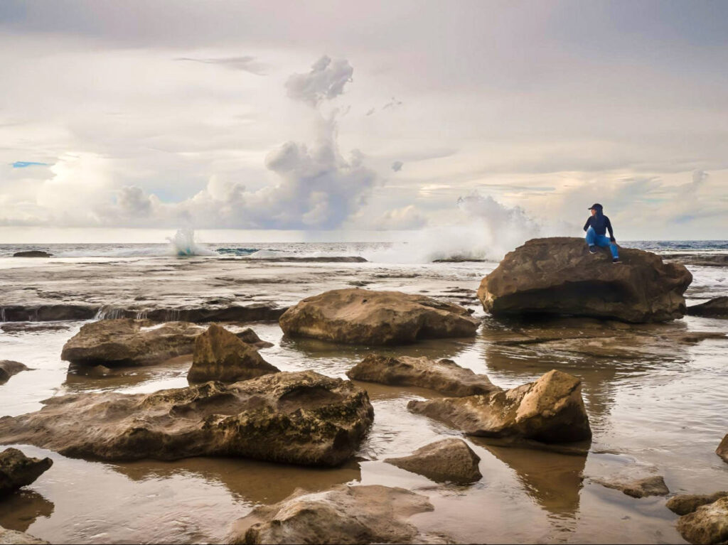 The author Vanessa Ramos, sitting on a rock overlooking the waves crashing to the shoreline at Pocita La Princesa