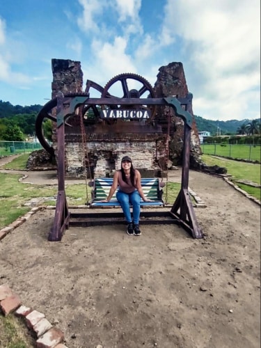 The author, Vanessa Ramos sitting on a swing with the sugar plantation ruins in the background