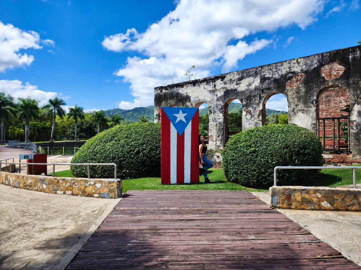 The author Vanessa Ramos, posing beside the Puerto Rican flag at Caguas Botanical Garden