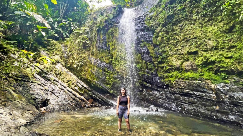 The author, Vanessa Ramos posing below the waterfalls in El Yunque National Rainforest