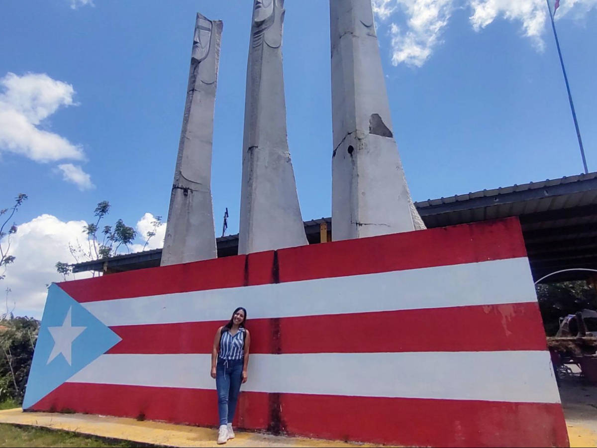 The author Vanessa Ramos posing in front of the huge Puerto Rico flag in Guavate