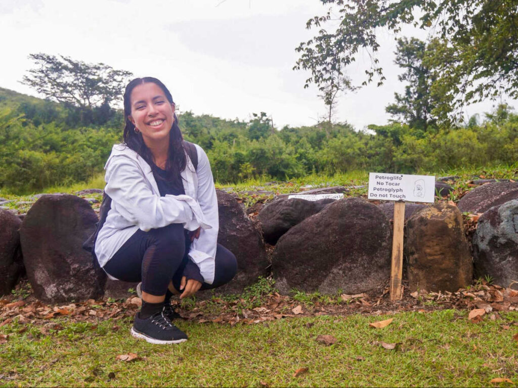 The author Vanessa smiling for a photo with the petroglyphs in Parque Ceremonial Tibes